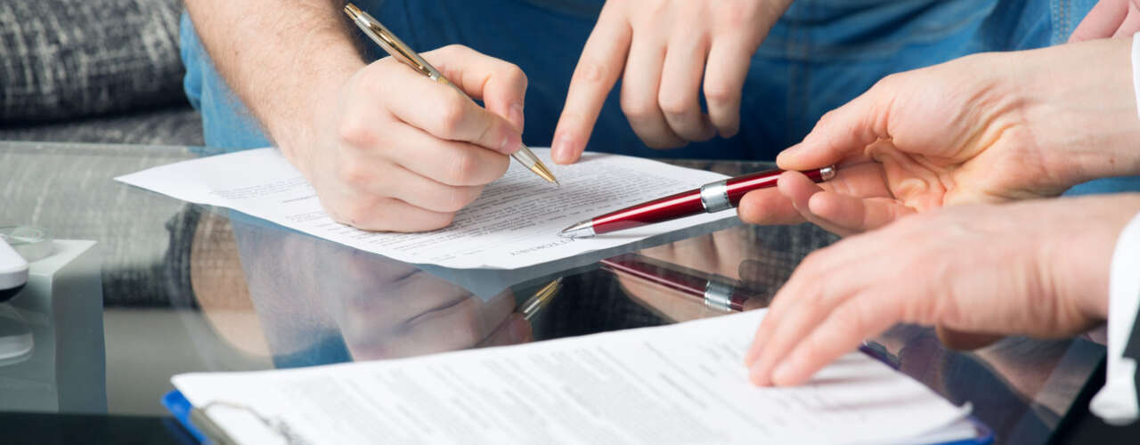 Hands of two men signed the document, sitting at the desk