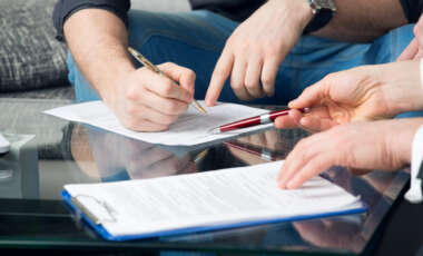 Hands of two men signed the document, sitting at the desk